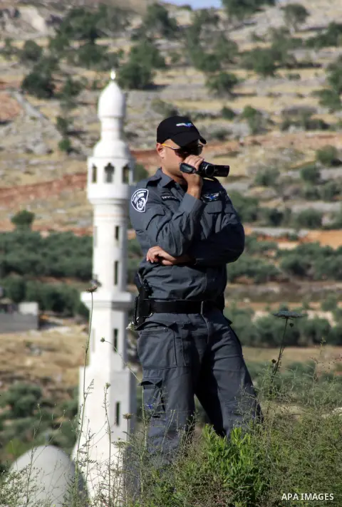 An Israeli policeman uses a video camera as Israeli army reservists take part in a demonstration against settlers' phenomenon of so-called "price tag" attacks, outside the Yitzhar Jewish settlement, near the West Bank ci...