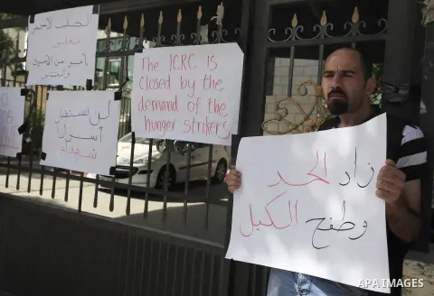 Palestinian activists hold banners outside the headquarters of the International Committee of the Red Cross (ICRC) in the West Bank city of Ramallah, on May 28, 2014. Protesters blocked the doors of the office and denied...