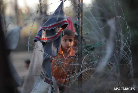 A photo taken on May 26, 2014, shows Palestinian children watch their relatives through a fence as they play football outside their homes, in Deir al-Balah in the central of Gaza Strip. Palestinians share a billion or mo...