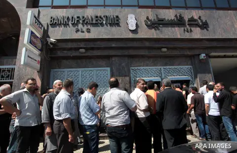 Palestinian employees wait in front of Bank of Palestine to withdrew their salaries from an ATM, in Gaza City on June 11, 2014. Palestinian police in Gaza Strip allowed banks to open after being closed for seven days fol...