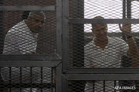 Australian journalist Peter Greste and Mohamed Fahmy stand inside court's cage as he waits to listen the ruling at a court in Cairo June 23, 2014. Three Al Jazeera journalists were jailed for seven years in Egypt on Mond...