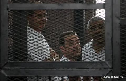 Al-Jazeera journalists stand inside court's cage as their wait to listen the ruling at a court in Cairo June 23, 2014. Three Al Jazeera journalists were jailed for seven years in Egypt on Monday after a court convicted t...