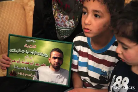 The son of Amer Abu Aysha holds his father's picture as he poses with his brother and his mother for media in their house in the West Bank city of Hebron June 27, 2014. Israel on Thursday named Abu Aysha as one of two le...