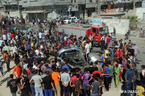 Palestinians gather around a car that was targeted by an Israeli air strike in Gaza City on June 27, 2014. The air strike killed two Palestinians, medics said, hours after a bomb exploded near troops manning Israel's sec...