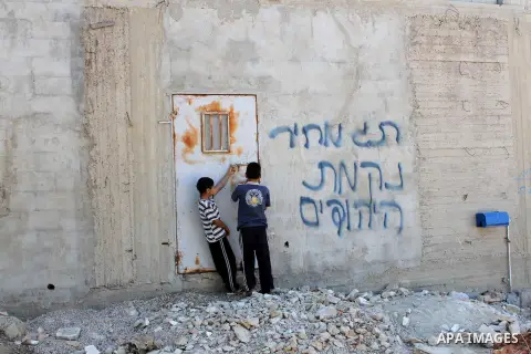Palestinian children stand near a wall showing the Hebrew writing words "blood vengeance" and "price tag" in the village of Aqraba southern the West Bank city of Nablus, on July 2, 2014. Photo by Nedal Eshtayah