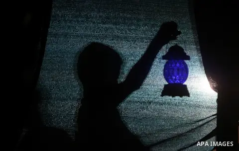 A Palestinian boy is seen behind a curtain holding a lantern behind on the third day of the Muslim fasting month of Ramadan, in Rafah in the southern Gaza Strip, on July 1, 2014. Muslims around the world celebrate Ramada...