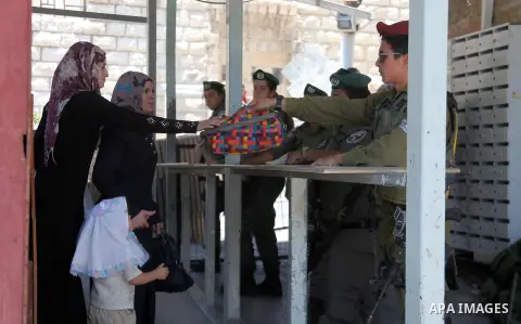 An Israeli police officer searches the bag of a Palestinian woman before reach the Ibrahimi mosque "Sanctuary of Abraham" to the traditional Friday prayers, the first of Islam's holy month of Ramadan, in the West Bank Ci...