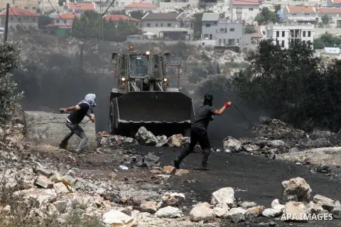 Palestinian protester throw stones towards an Israeli bulldozer during clashes following a weekly protest against the expropriation of Palestinian land by Israel in the West Bank village of Kfar Qaddum, near Nablus on Ju...