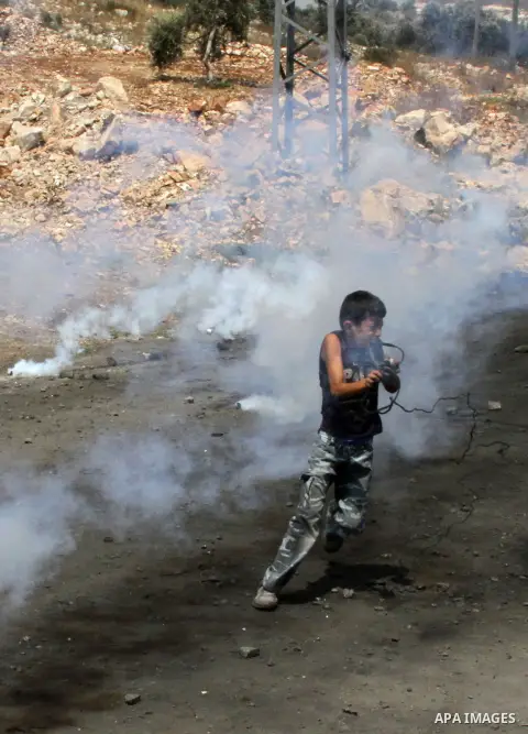 A Palestinian boy runs for cover from tear gas fired by Israeli security forces during clashes following a weekly protest against the expropriation of Palestinian land by Israel in the West Bank village of Kfar Qaddum, n...
