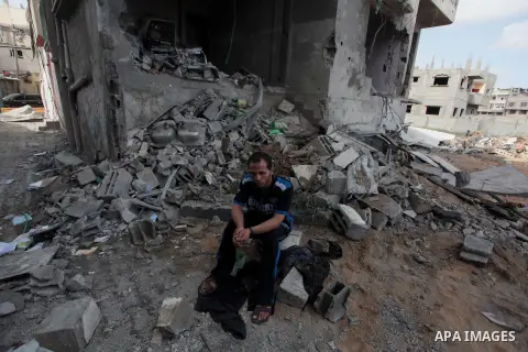 A Palestinian man sits amidst the debris of a neighbouring house which police said was damaged after an Israeli air strike destroyed Tayseer Al-Batsh's family house, in Gaza City July 13, 2014. The Israeli air strike on...