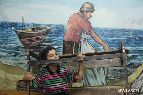 A displaced Palestinian boy from Beit Hanun in the northern Gaza Strip stands on July 23, 2014 in front of a mural painting at a UN school in thre refugee camp of Jabalia where displaced families have taken refuge after...