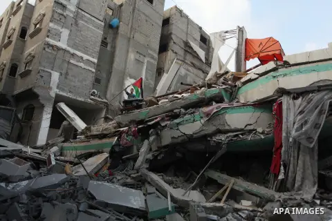 A Palestinian man displays national flags, Islamist Hamas movement flags and portraits of Hamas top leader in Gaza, Ismail Haniya, on the rubble of the latter's house after it was hit by an overnight Israeli air strike,...