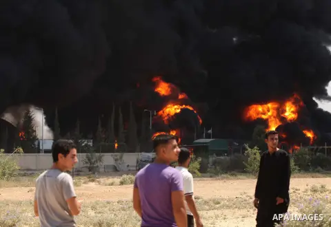 Palestinian men stand looking as flames engulf the fuel tanks of the only power plant supplying electricity to the Gaza Strip after it was hit by overnight Israeli shelling, on July 29, 2014, in the south of Gaza City. T...
