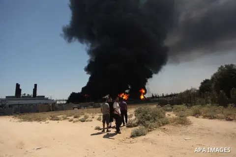 Palestinian men stand looking as flames engulf the fuel tanks of the only power plant supplying electricity to the Gaza Strip after it was hit by overnight Israeli shelling, on July 29, 2014, in the south of Gaza City. T...