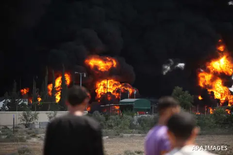 Palestinian men stand looking as flames engulf the fuel tanks of the only power plant supplying electricity to the Gaza Strip after it was hit by overnight Israeli shelling, on July 29, 2014, in the south of Gaza City. T...