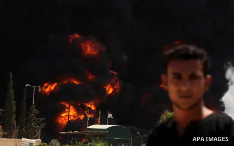 Palestinian men stand looking as flames engulf the fuel tanks of the only power plant supplying electricity to the Gaza Strip after it was hit by overnight Israeli shelling, on July 29, 2014, in the south of Gaza City. T...