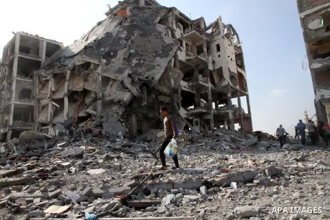 A Palestinian carries his belonging as he walks past a badly damaged residential building after returning to Beit Lahiya town, which witnesses said was heavily hit by Israeli shelling and air strikes during the Israeli o...