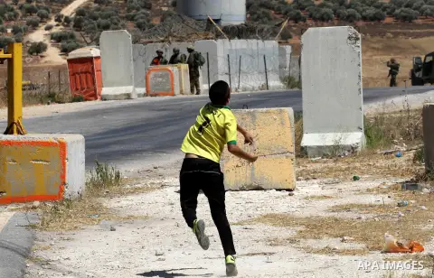 A Palestinian protester throws stones towards Israeli soldiers during clashes following a demonstration against the Israeli military action in Gaza, at the Beit Fourik checkpoint near the West Bank of Nablus on Friday, A...