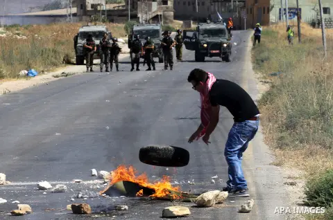 A Palestinian protester burn a tire during clashes with Israeli soldiers following a demonstration against the Israeli military action in Gaza, at the Beit Fourik checkpoint near the West Bank of Nablus on Friday, August...