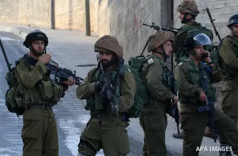 Israeli soldiers stand guard as Palestinians evacuate the family of Zakariyya al-Aqra, 24, who was reportedly shot dead by Israeli soldiers, from his house in the West Bank village of Qabalan, near Nablus on August 11, 2...