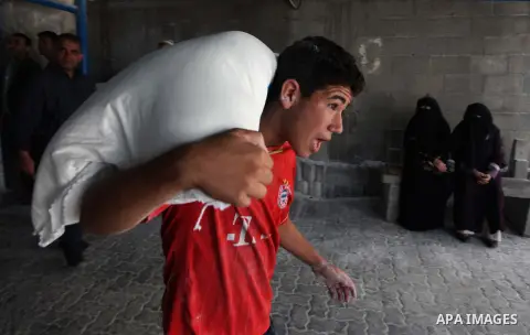 A Palestinian man carries bags of flour he received at a distribution centre of the United Nations Relief and Works Agency (UNRWA) in Gaza City on August 11, 2014. An Israeli delegation arrived in Cairo for indirect nego...