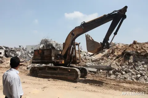 A Palestinian man looks as a bulldozer removes rubbles from a mosque which witnesses said was destroyed by an Israel air strike during the offensive, on the second day of a five-day ceasefire, in Gaza city on August 15,...