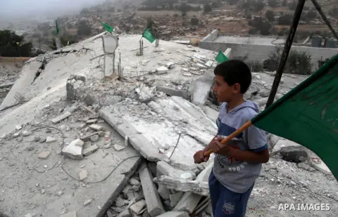 A Palestinian boy holds a national flag as he stands on the rubble of a Hossam Al-Qawasmi house's destroyed by Israeli army, in the West Bank city of Hebron on August 18, 2014. The Israel Defense Forces demolished the ho...