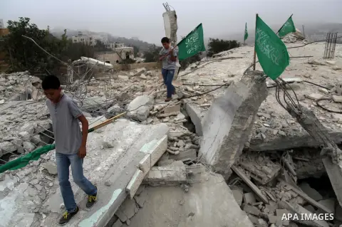 Palestinian boys hold national flags as they stand on the rubble of a Hossam Al-Qawasmi house's destroyed by Israeli army, in the West Bank city of Hebron on August 18, 2014. The Israel Defense Forces demolished the home...