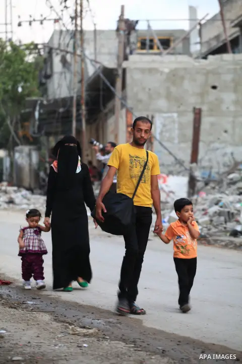 A group of Palestinians carry some of their belonging as they walk past a destroyed home, back to a UN school where many displaced Palestinians are taking refuge, in the Shejaiya neighborhood of Gaza City, on August 18,...