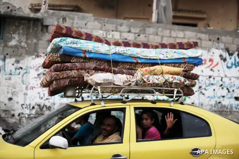 A group of Palestinians carry some of their belonging as they walk past a destroyed home, back to a UN school where many displaced Palestinians are taking refuge, in the Shejaiya neighborhood of Gaza City, on August 18,...