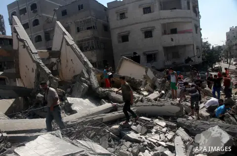 Palestinians gather around the remains of a tower building housing offices which witnesses said was destroyed by an Israeli air strike in Gaza City August 26, 2014. Israeli air strikes launched before dawn on Tuesday kil...