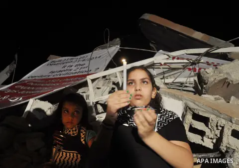 Palestinian Families hold candles during a protest in front of the remains El Zafer Tower destroyed in an israeli airstrike, in Gaza city, on Aug. 27, 2014. The open-ended ceasefire in the Gaza war between Israel and the...