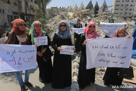 Palestinian women hold banners as they take part a protest in front of the El-Basha Tower destroyed by Israeli airstrike in Gaza city on August 28, 2014. Israel and Palestinians both boasted of victory in the Gaza war bu...