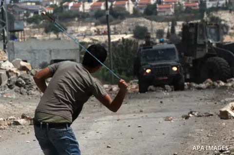 Palestinian protester hurls stones at Israeli soldiers during weekly clashes over the Jewish settlement of Qadomem at Kofr Qadom village, near West Bank city of Nablus, 29 August 2014. Photo by Nedal Eshtayah