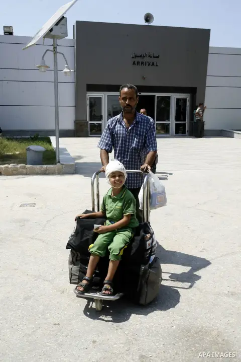A Palestinian father wheels his wounded son as they wait to be given the permission to cross into Egypt at the Rafah border crossing in the southern Gaza Strip, on August 28, 2014. The Rafah crossing with Egypt is Gaza's...