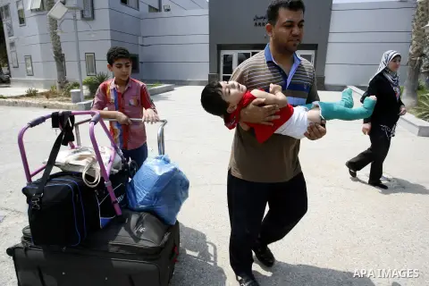 A Palestinian father carries his wounded son as they wait to be given the permission to cross into Egypt at the Rafah border crossing in the southern Gaza Strip, on August 28, 2014. The Rafah crossing with Egypt is Gaza'...