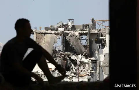 A Palestinian man sits past buildings destroyed during fighting between Hamas militants and Israel in the Al-Shaaf neighbourhood, in Gaza City, on August 31, 2014. An indefinite ceasefire to end seven weeks of fighting b...
