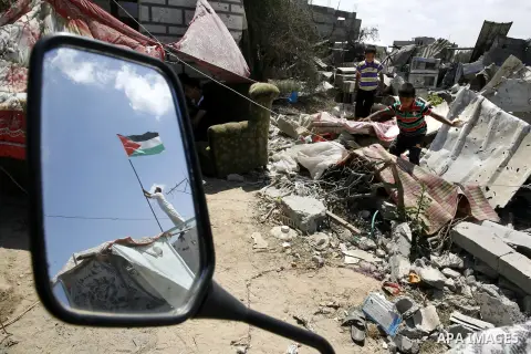 A Palestinian man holds a national flag to hang on the rubble of as children search in a destroyed house in Khan Yunis in the southern Gaza Strip on September 11, 2014. Israel's deputy foreign minister,Tzahi Hanegbi , wa...