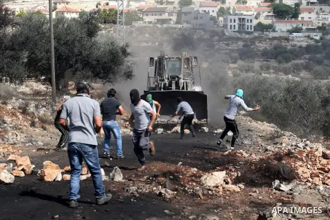 Palestinian protesters throw stones towards an Israeli bulldozer during clashes following a protest in the village of Kfar Qaddum, near the northern city of Nablus, in the occupied West Bank on October 03, 2014. Photo by...