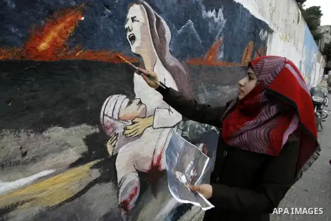 A Palestinian girl paints a mural on a wall depicts a woman crying as she holds her killed husband referring to the Israeli offensive seven weeks, in Rafah in the southern Gaza Strip, October 5, 2014. Israel opened the b...