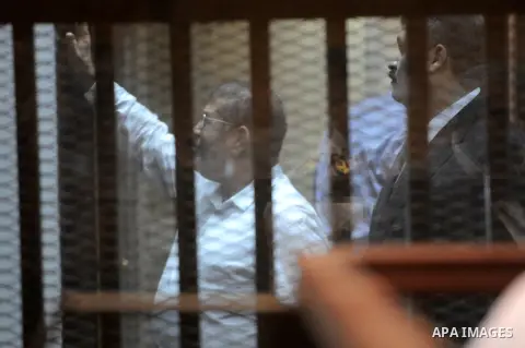 Egypt's deposed Islamist president Mohamed Morsi gestures inside the defendant's cage during his trial in Cairo on October 29, 2014. Ousted president Mohamed Morsi’s 'Prison Break' trial which took place Wednesday has be...