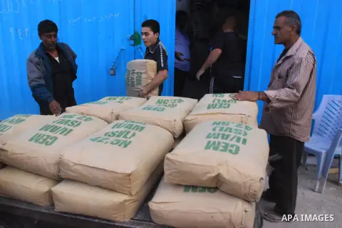 Palestinian workers carry bags of cement as Palestinians, whose houses were partially damaged by what witnesses said was Israeli shelling during the most recent conflict between Israel and Hamas, wait to receive cement o...