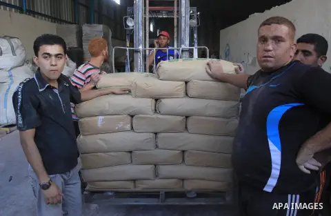 Palestinian workers carry bags of cement as Palestinians, whose houses were partially damaged by what witnesses said was Israeli shelling during the most recent conflict between Israel and Hamas, wait to receive cement o...