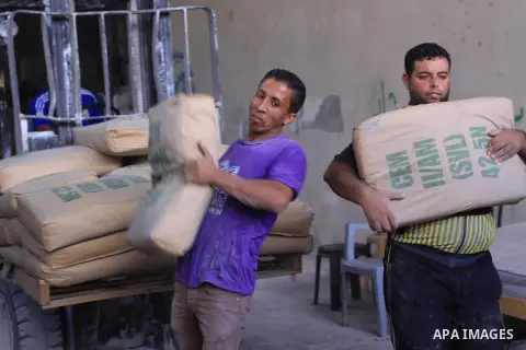 Palestinian workers carry bags of cement as Palestinians, whose houses were partially damaged by what witnesses said was Israeli shelling during the most recent conflict between Israel and Hamas, wait to receive cement o...