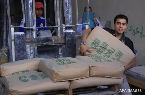 Palestinian workers carry bags of cement as Palestinians, whose houses were partially damaged by what witnesses said was Israeli shelling during the most recent conflict between Israel and Hamas, wait to receive cement o...