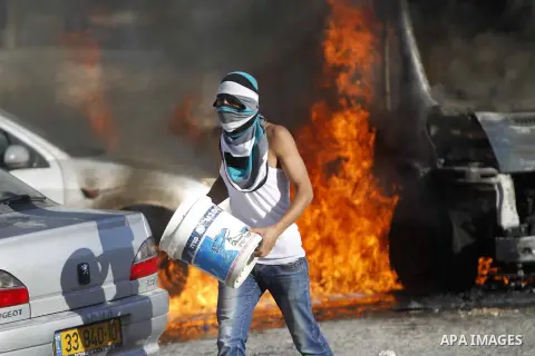 A masked Palestinian youth tries to extinguish the fire in cars during clashes with Israeli security forces after Moataz Higazi was shot in east Jerusalem October 30, 2014. Israeli police shot and killed Higazi suspected...