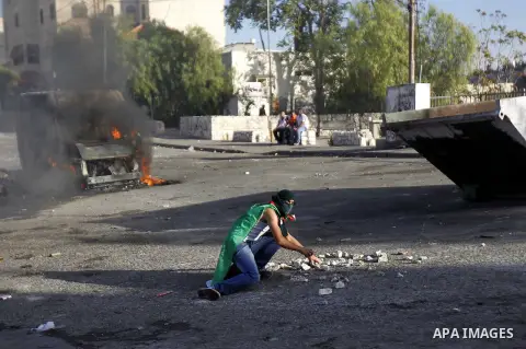 A masked Palestinian youth throw stones at Israeli security forces during clashes after Moataz Higazi was shot in east Jerusalem October 30, 2014. Israeli police shot and killed Higazi suspected of trying to kill a hard-...