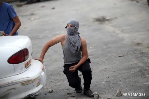 A Palestinian protester takes cover during clashes with Israeli security forces at the Qalandia checkpoint between Ramallah and Jerusalem City following a rally against the restrictions on the Al-Aqsa mosque compound on...
