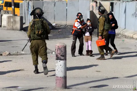 A member of Palestinian medics covers girl's face from tear gas fired by Israeli security forces during clashes with Palestinian protester at the Qalandia checkpoint between Ramallah and Jerusalem City following a rally...