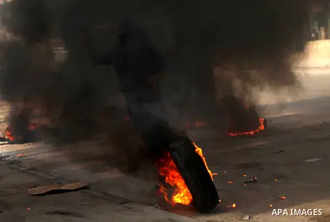 A Palestinian protester kicks a burning tire during clashes with Israeli security forces at the Qalandia checkpoint between Ramallah and Jerusalem City following a rally against the restrictions on the Al-Aqsa mosque com...